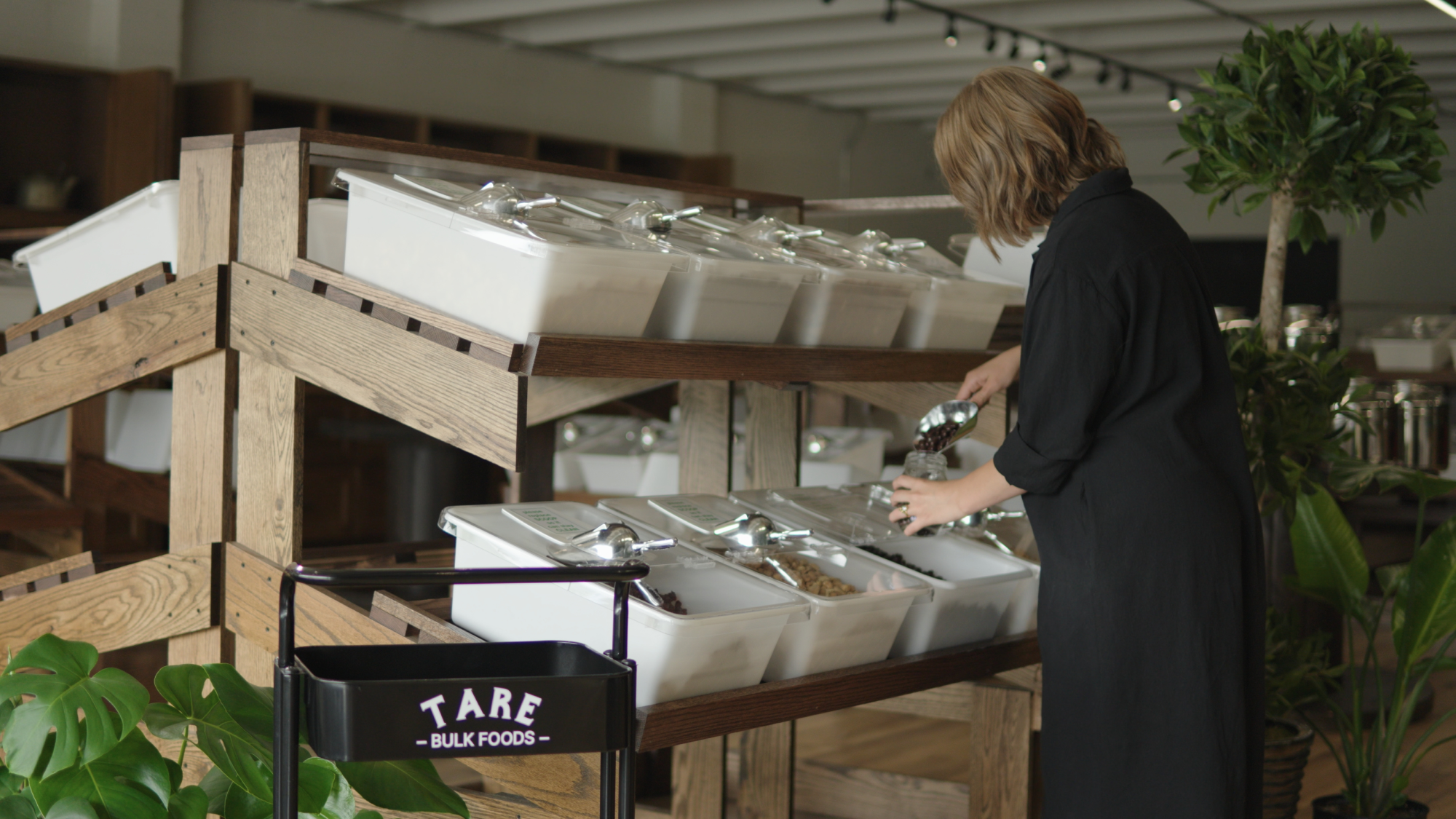 Person scooping bulk food from bins on wooden shelves